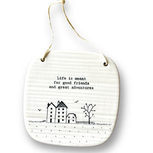 Square porcelain plaque with a picture of three buildings and a tree with the words 'Life is meant for good friends and great adventures'